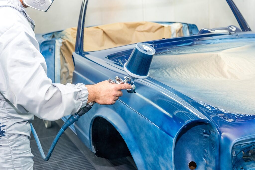 Car full respray with blue paint by man in white boiler suit